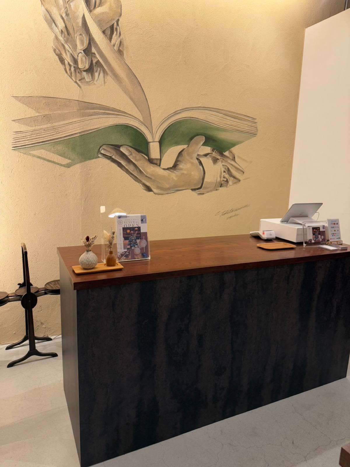カウンター奥の壁画。本を開く手 / The mural behind the counter: a hand opening a book