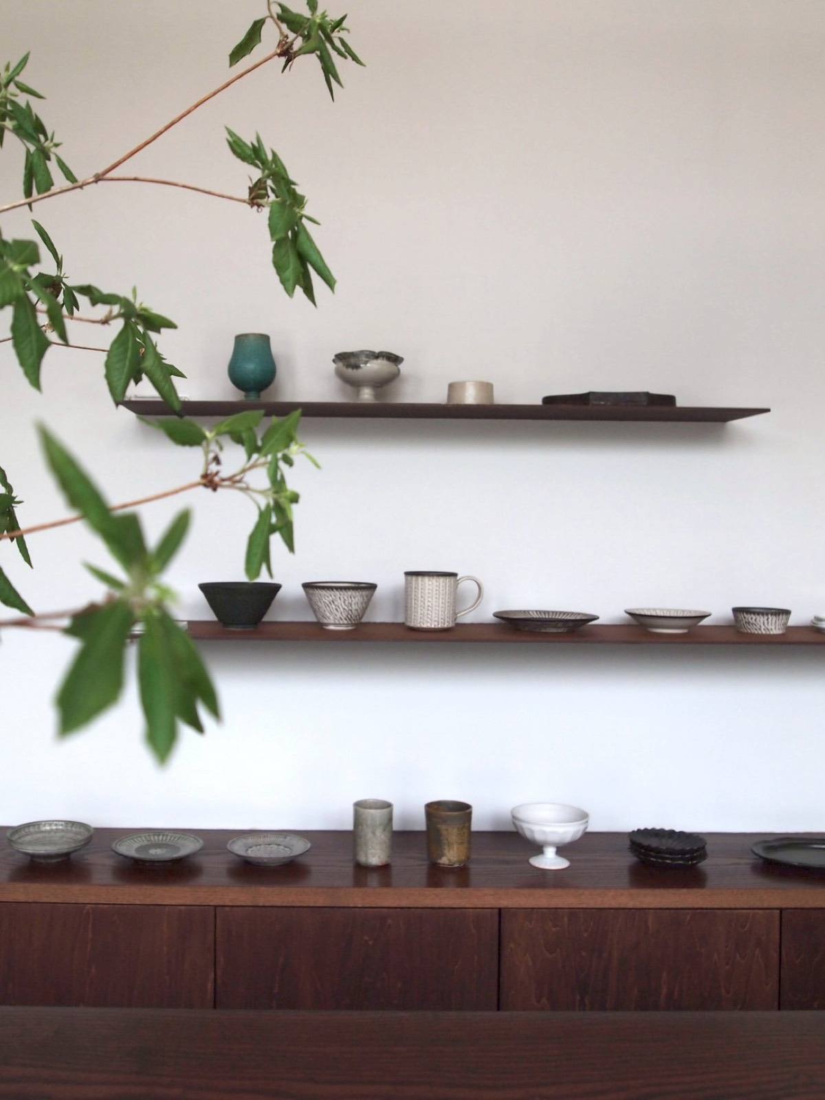 青葉ごしの白い壁と浮き棚 / Floating shelves of pottery behind green leaves