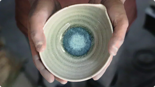 両手で包まれた片口。細かい貫入の入った藁灰釉の見込みに、青い釉だまりが円く広がる