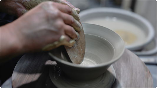轆轤の上で、木のコテを当てて鉢の内側を整える作り手の手元