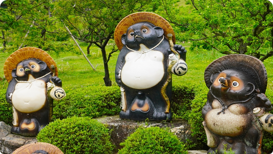 庭に並ぶ信楽たぬきの陶像3体。笠をかぶり、徳利と通い帳を手にした姿