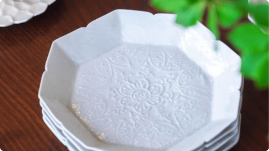 Stacked white porcelain octagonal plates by Maeda Asami, a floral relief pressed into the centre of the top plate