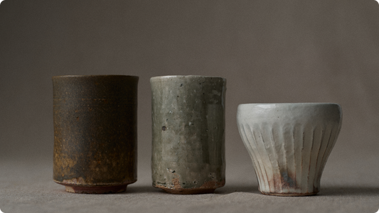 Three cups side by side: an unglazed yakishime brown, an ash-glazed grey-green, and a white kohiki with carved shinogi ridges