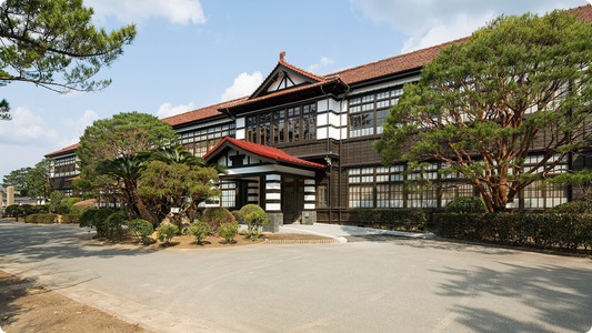 萩・明倫学舎の本館棟を正面から。赤瓦の屋根と白壁が続く木造2階建ての旧校舎で、中央に車寄せがあり、前庭に松が植わる