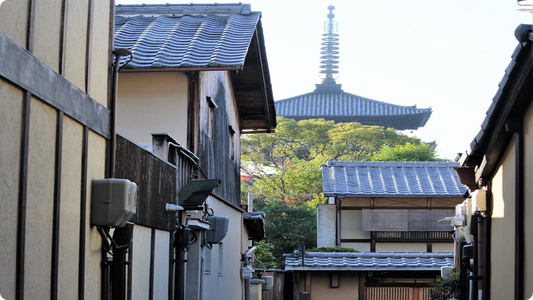 A narrow Kyoto lane lined with tiled roofs, the five-storey Yasaka Pagoda rising above the trees in Higashiyama