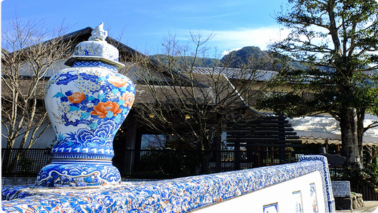 Large blue-and-white porcelain jar with orange peony painting standing outdoors in Imari, in front of a wall faced with hand-painted ceramic tiles