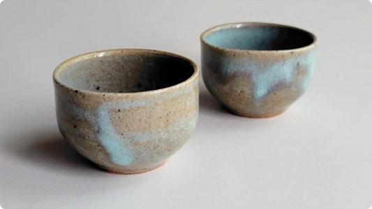 Two small stoneware cups with pale turquoise ash glaze pooling in patches over sandy speckled clay