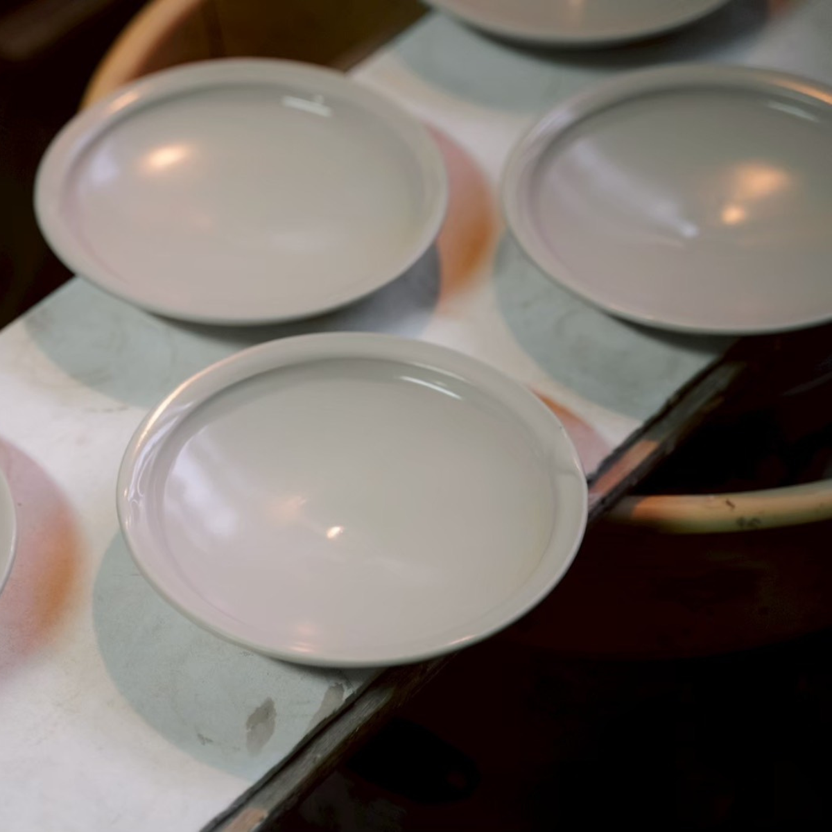 White-rimmed plates resting on a workbench in a Kyoto studio, still glossy from glazing
