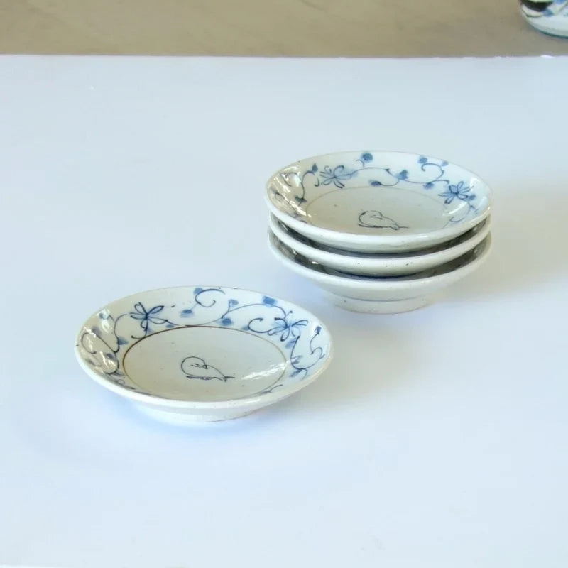 Four small blue and white plates with a vine border and a sketched bird, three stacked and one in front