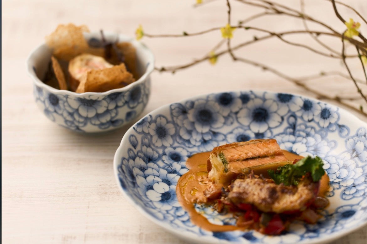 Blue and white floral porcelain — a shallow plate of grilled salmon beside a lobed bowl, on pale wood