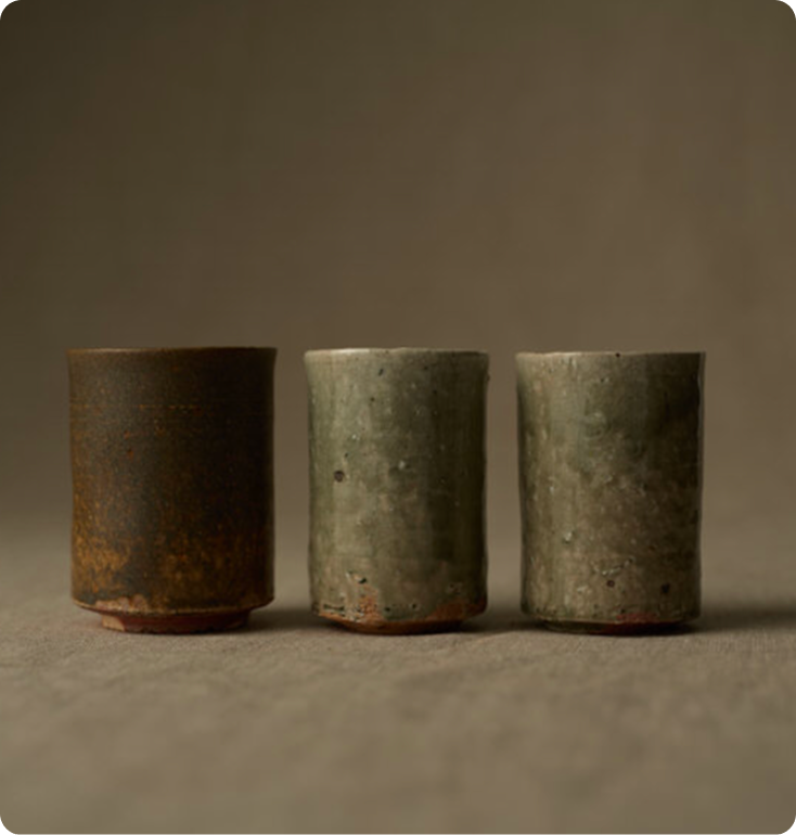 並べられた3つの湯呑み。左は焦げ茶色の鉄釉、中央と右はオリーブグリーンの灰釉が施された湯呑み。