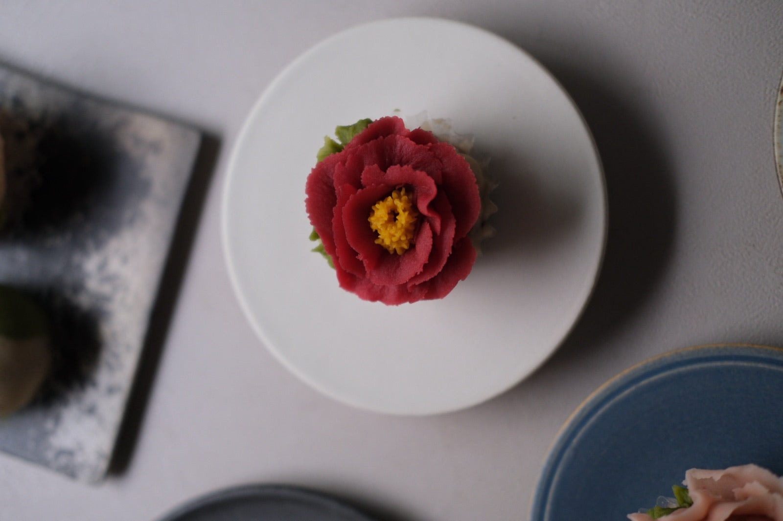 白い小皿にのせた、赤い花の練り切り / A red flower-shaped nerikiri sweet on a small white plate