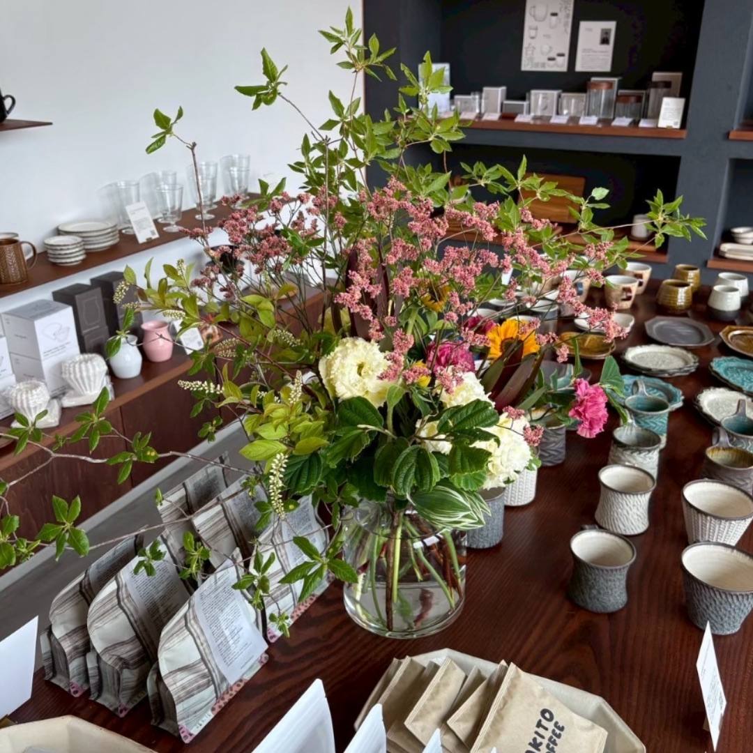 季節の花を生けたガラスの花器と、並ぶカップ / Seasonal flowers in a glass vase among rows of cups