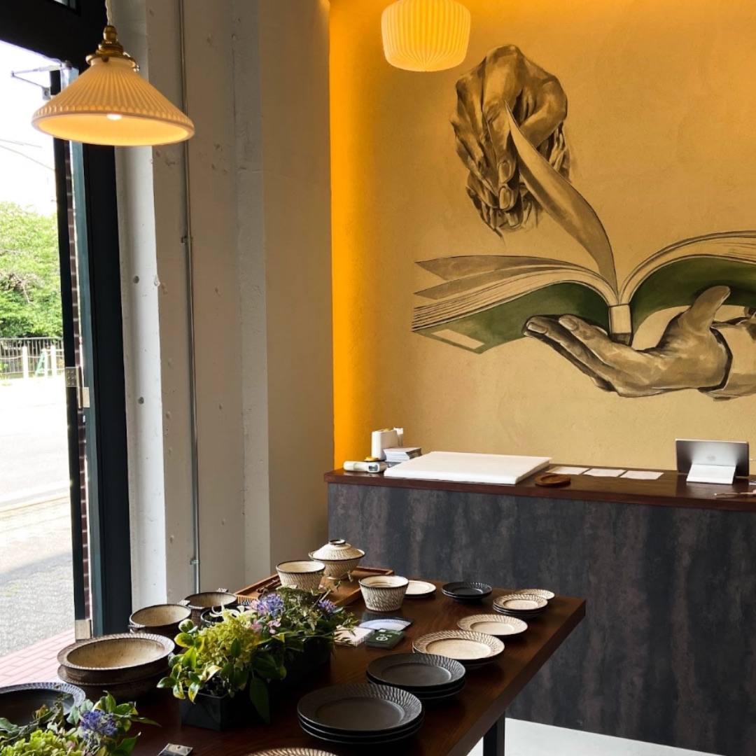 壁画と吊り灯りの下、鎬の器が並ぶ卓 / Ribbed plates and bowls on a long table beneath the mural and pendant lamps