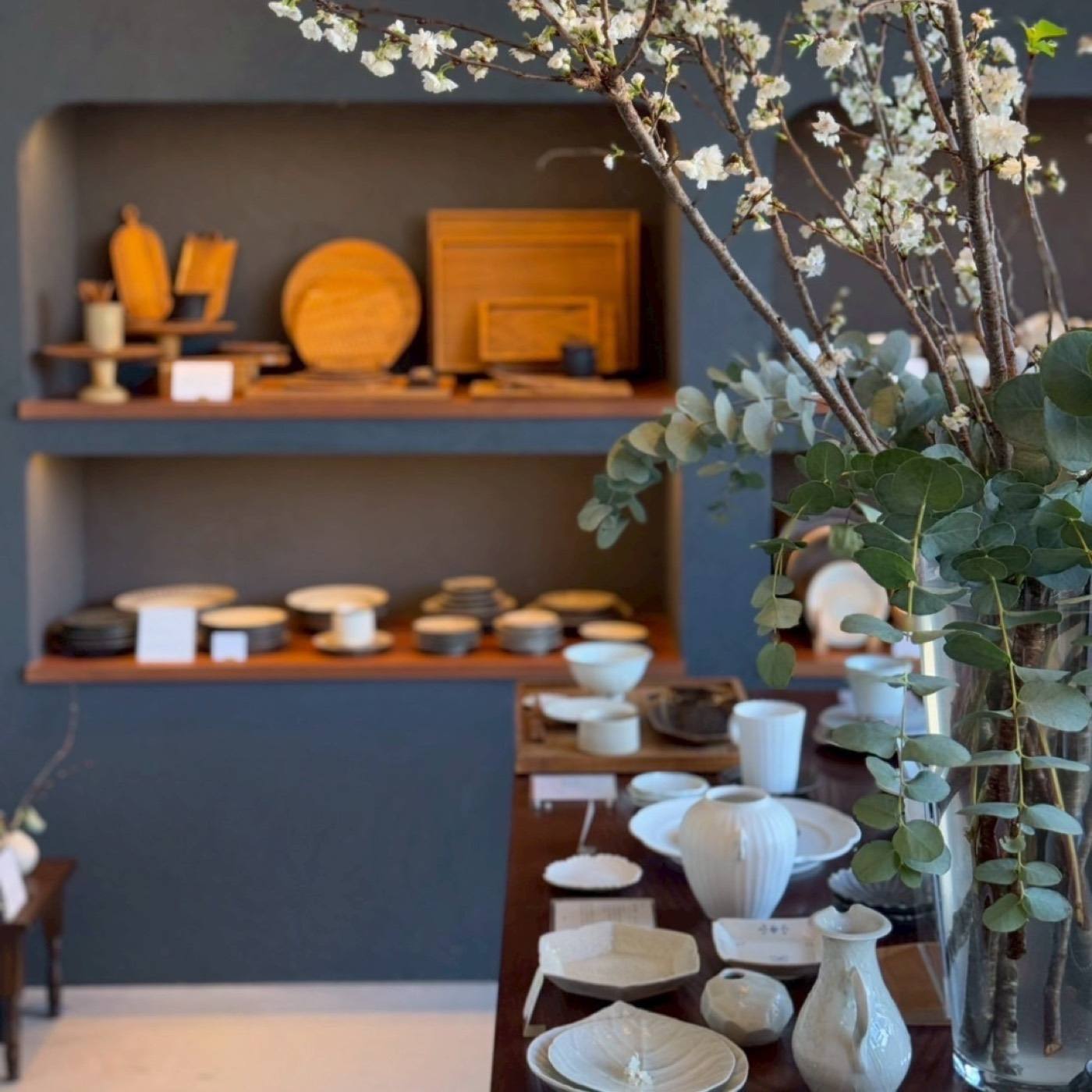 桜の枝を生けた店内と白い器 / Cherry branches above a table of white ceramics