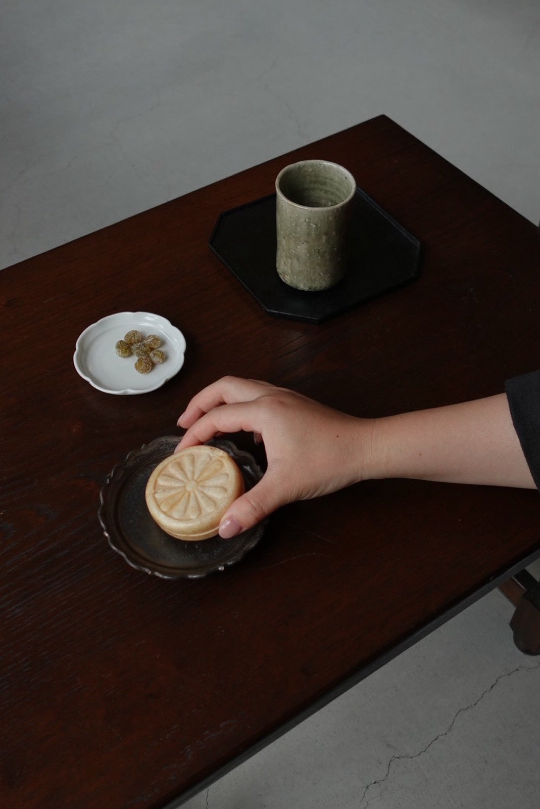 輪花の小皿から菊の和菓子を取る手 / A hand lifting a chrysanthemum sweet from a scalloped plate